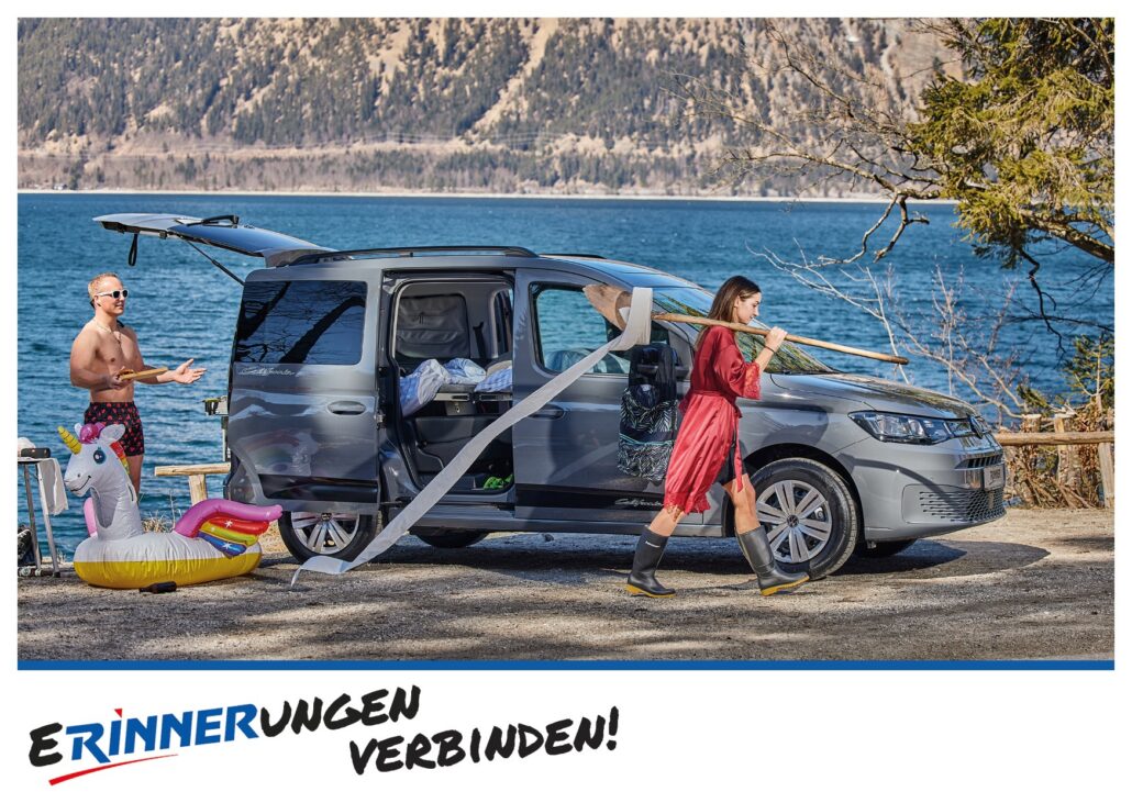 Werbepostkarte für Autohaus Rinner mit VW Caddy am See, einer Frau mit Schaufel und einem aufblasbaren Einhorn. Darunter der Slogan „Erinnerungen verbinden!“.